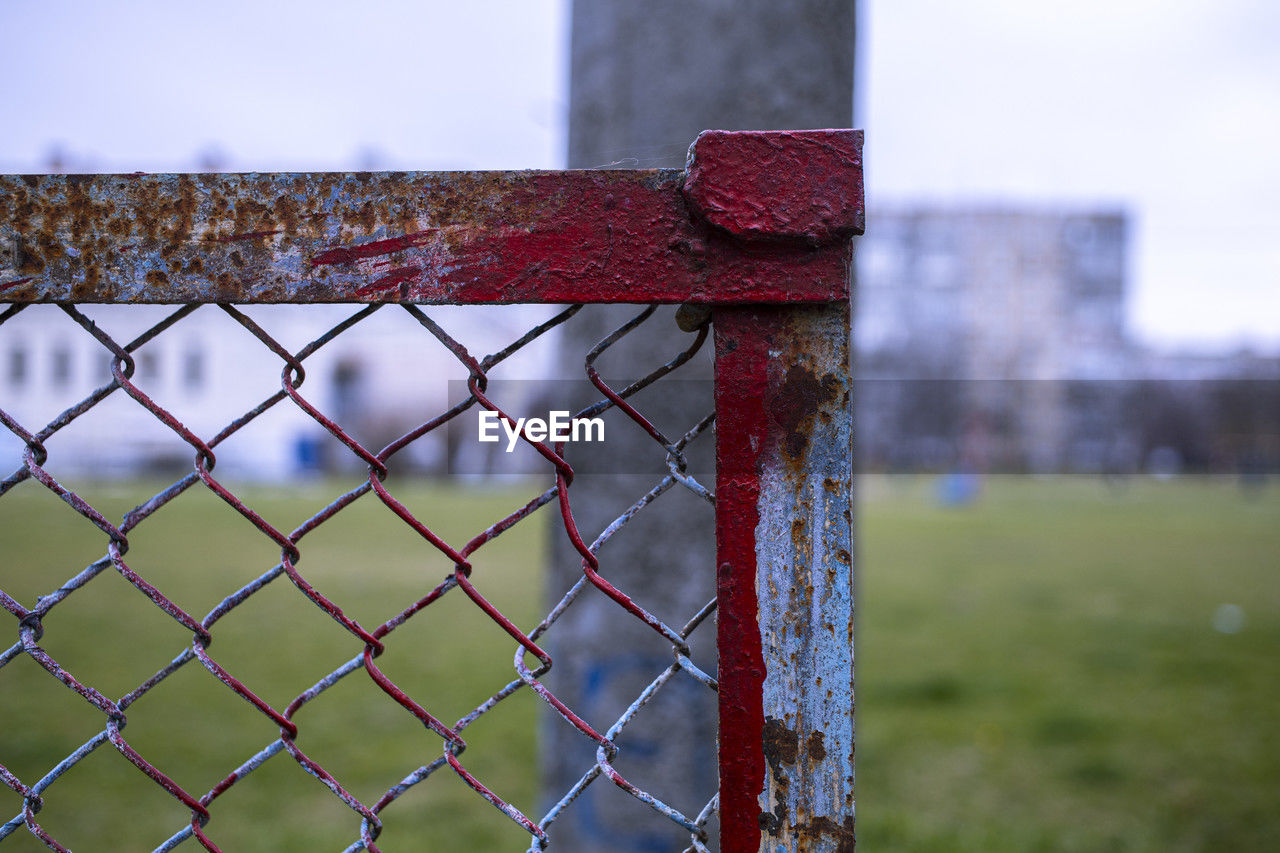 fence, sports, grass, focus on foreground, chainlink fence, security, protection, no people, metal, day, nature, outdoor structure, red, outdoors, green, close-up, playing field, net, sky, chain-link fencing, wire fencing, architecture, team sport, wall