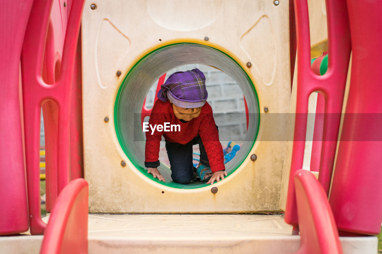 Full length of cute girl kneeling in outdoor play equipment in playground