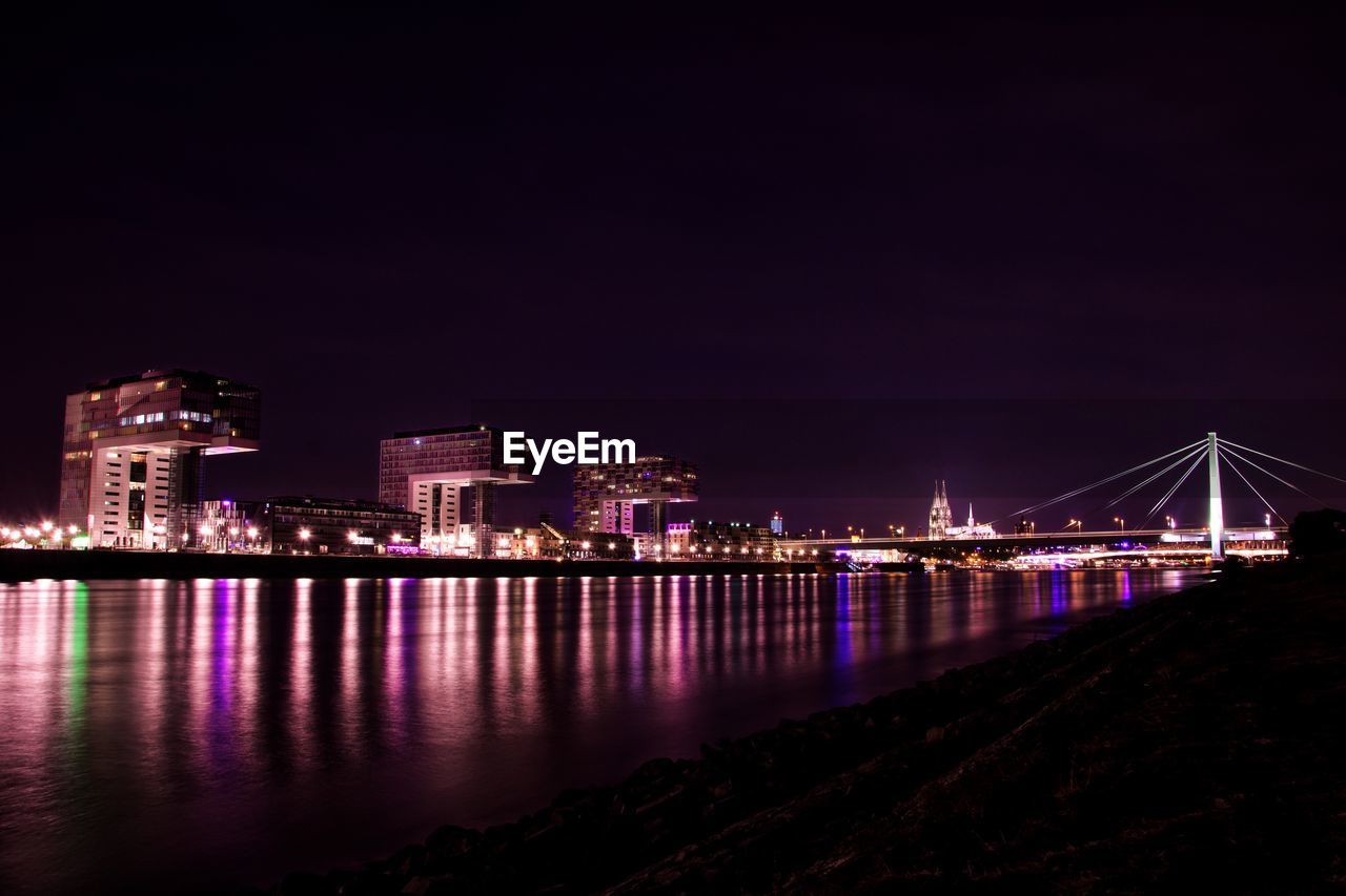 Illuminated city by river against sky at night