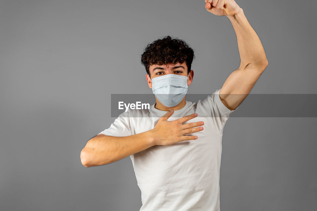 portrait of young man with arms raised standing against gray background