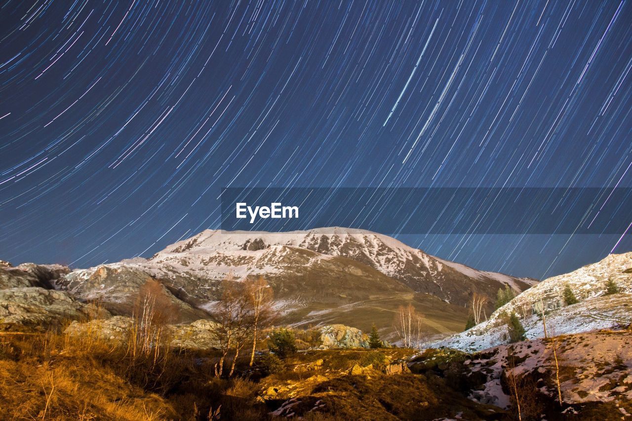 Scenic view of snow covered mountains against star trails