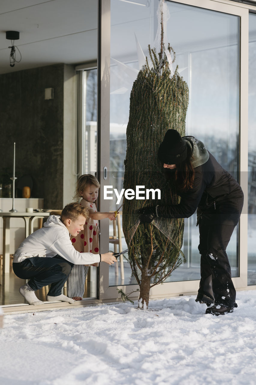 Woman with children preparing christmas tree in front of house