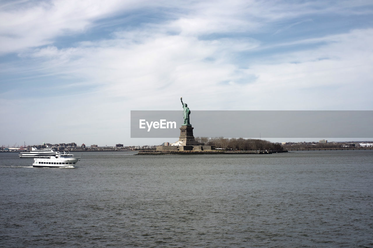 Statue of liberty in city against cloudy sky