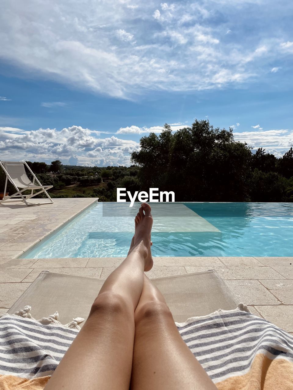 Low section of woman relaxing at pool against sky