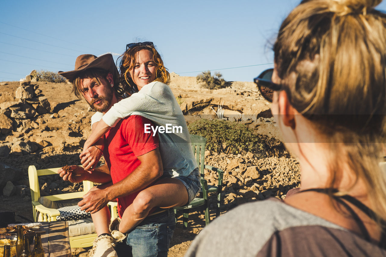 Rear view of woman looking at friends piggybacking against sky