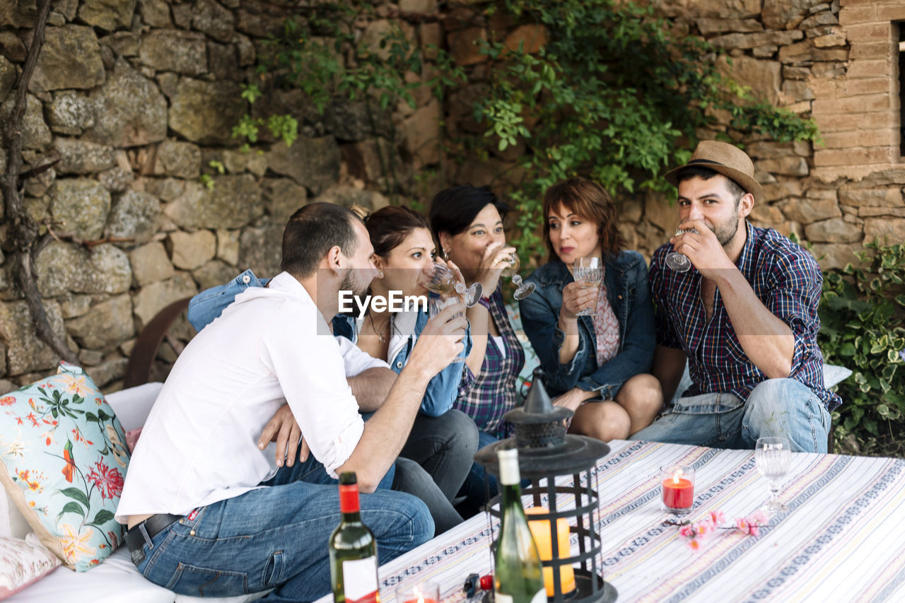 Happy friends drinking wine at party against stone wall