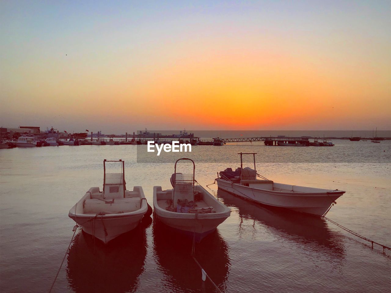 BOATS MOORED IN SEA AGAINST ORANGE SKY