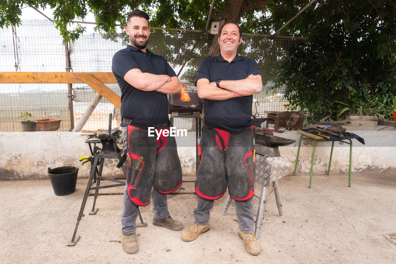 Portrait of smiling blacksmiths standing at workshop