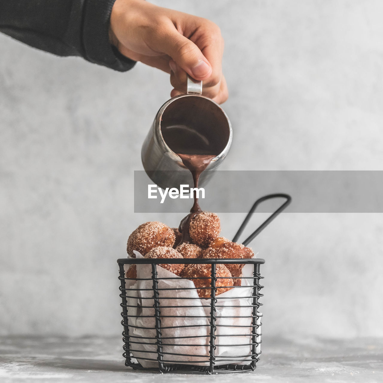 Chocolate being poured over donut holes churros on table against wall