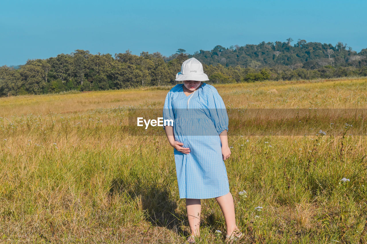 plant, grassland, field, prairie, one person, adult, meadow, landscape, land, agriculture, natural environment, nature, rural scene, hat, rural area, clothing, environment, grass, sky, person, full length, standing, growth, farm, day, occupation, blue, senior adult, walking, men, crop, outdoors, lifestyles, farmer, pasture, beauty in nature, plain, casual clothing, sunlight, leisure activity, scenics - nature, rear view, women, green, steppe