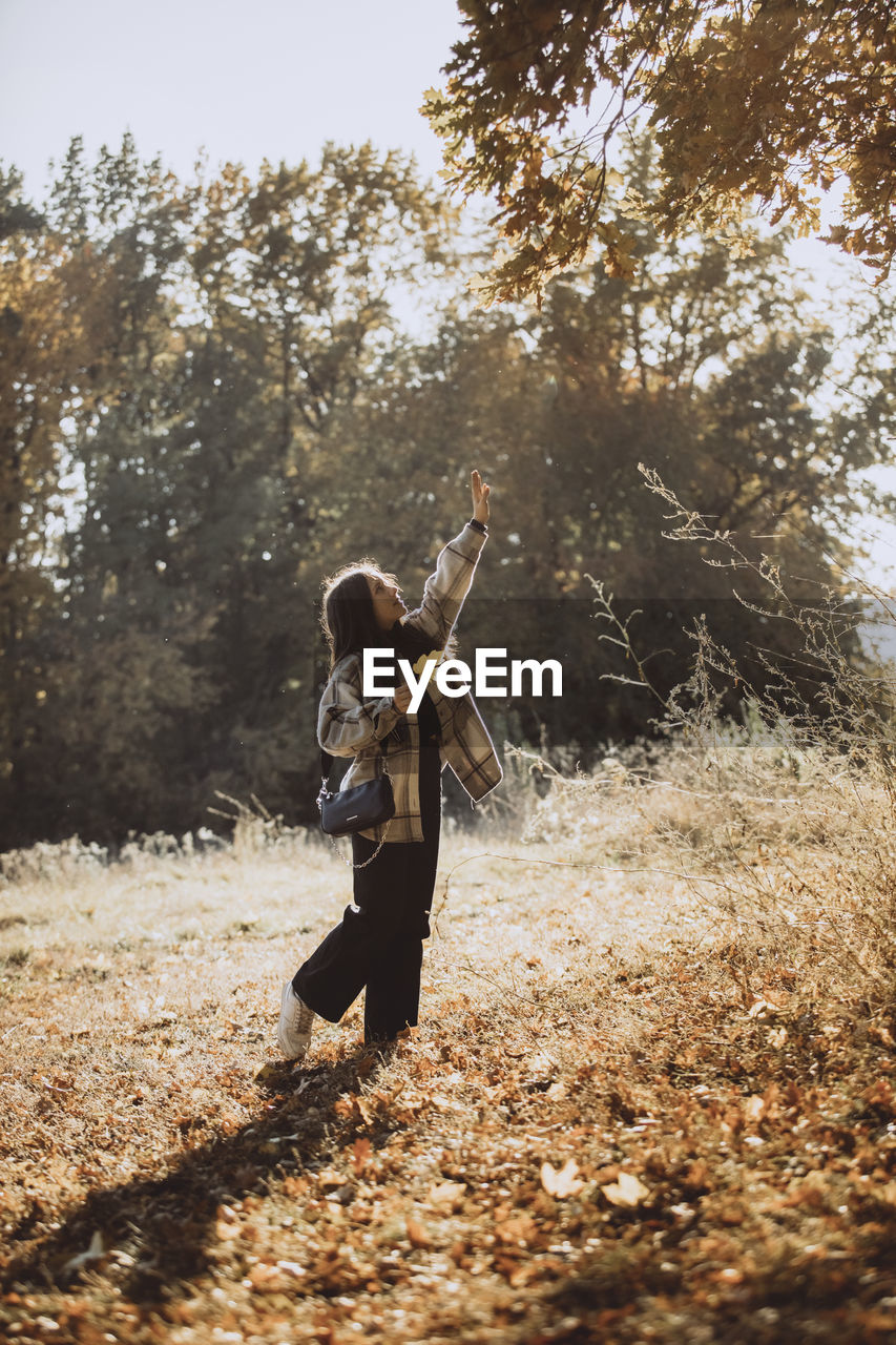 Girl with hand raised standing in autumn forest