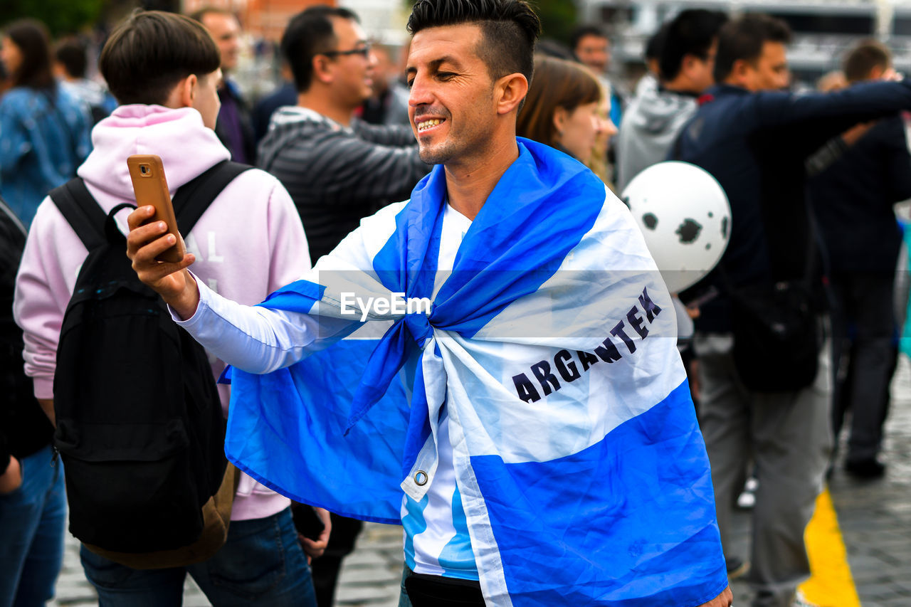 Man wearing argentinian flag while taking selfie outdoors