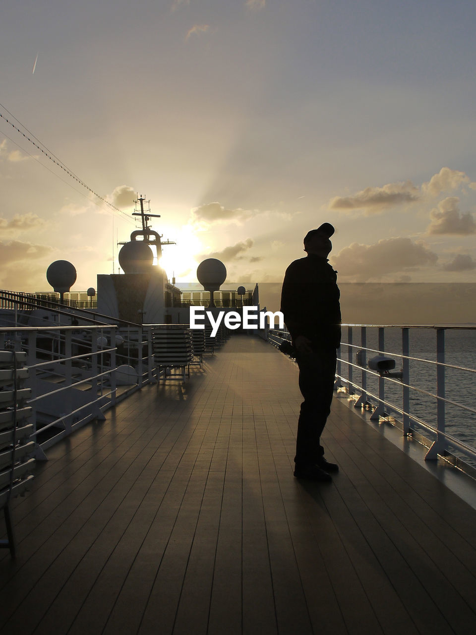 REAR VIEW OF MAN STANDING BY RAILING AGAINST SKY