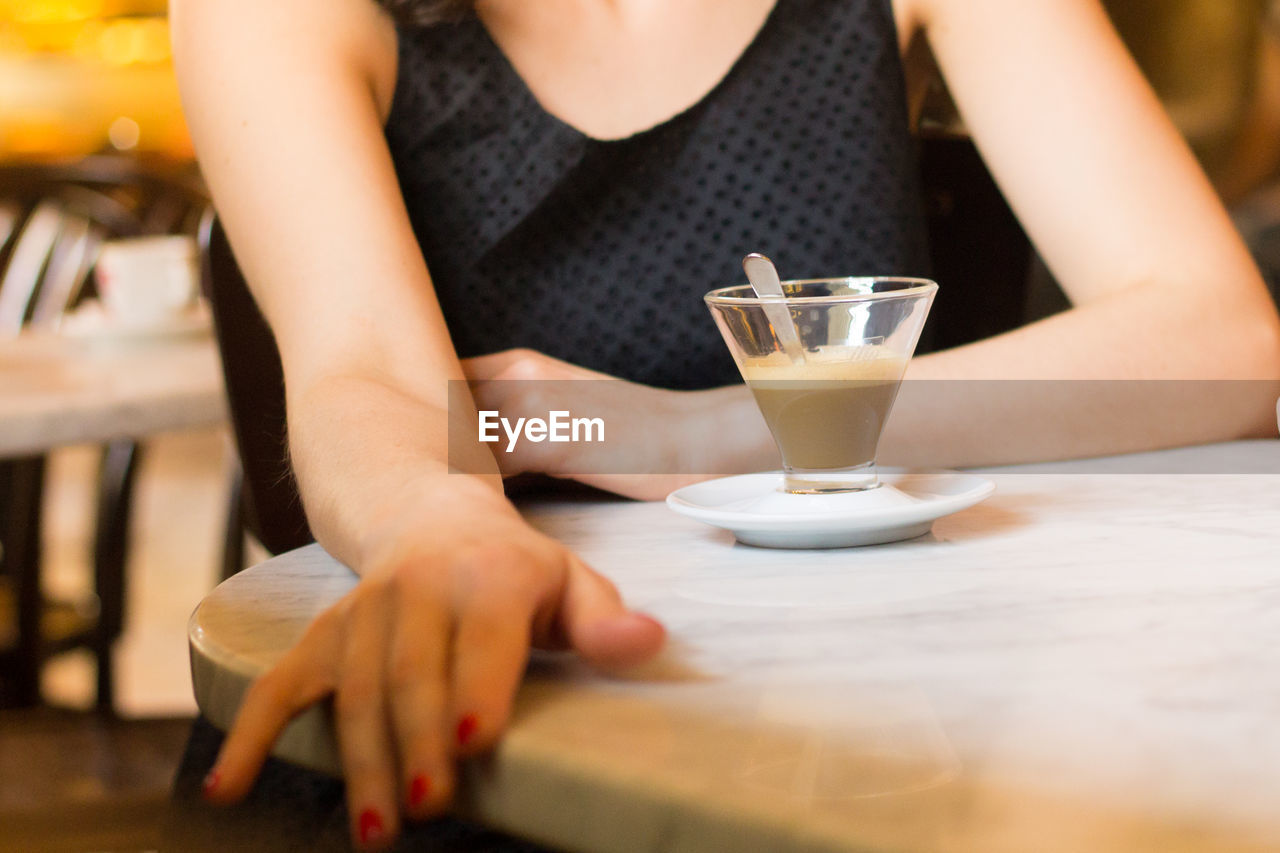 MIDSECTION OF WOMAN HOLDING GLASS OF TABLE