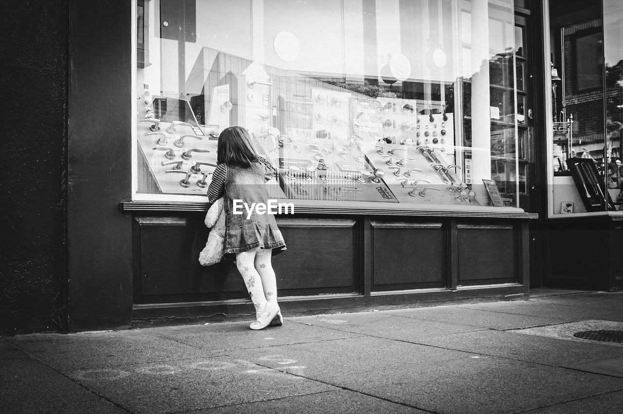 Full length of girl peeking in store through glass window