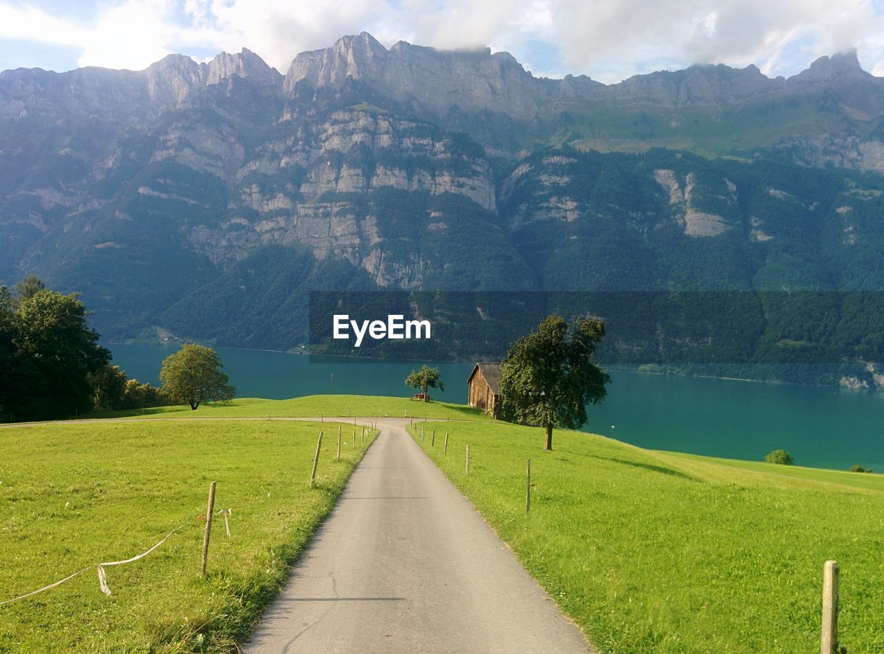 Empty road amidst grassy field by walensee against swiss alps