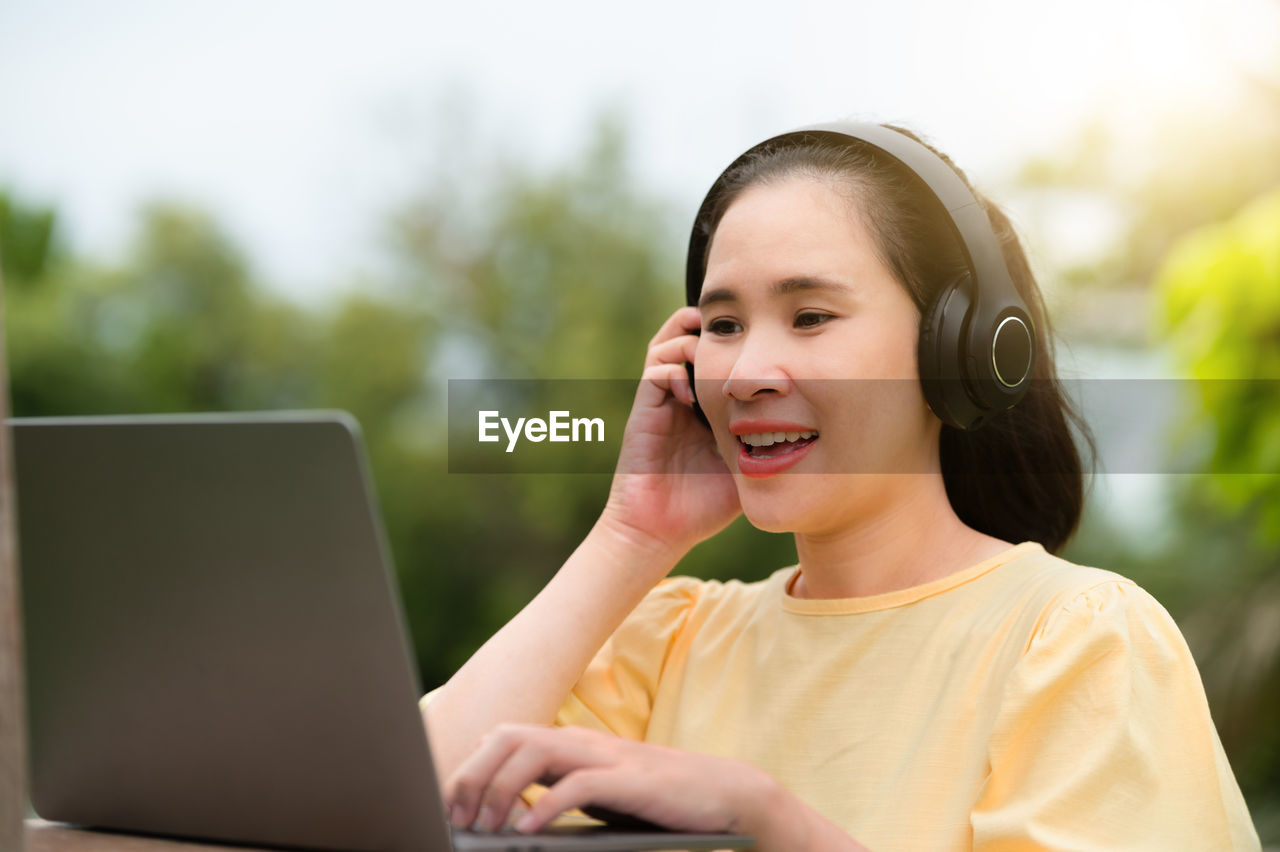 PORTRAIT OF SMILING WOMAN USING MOBILE PHONE IN PARK