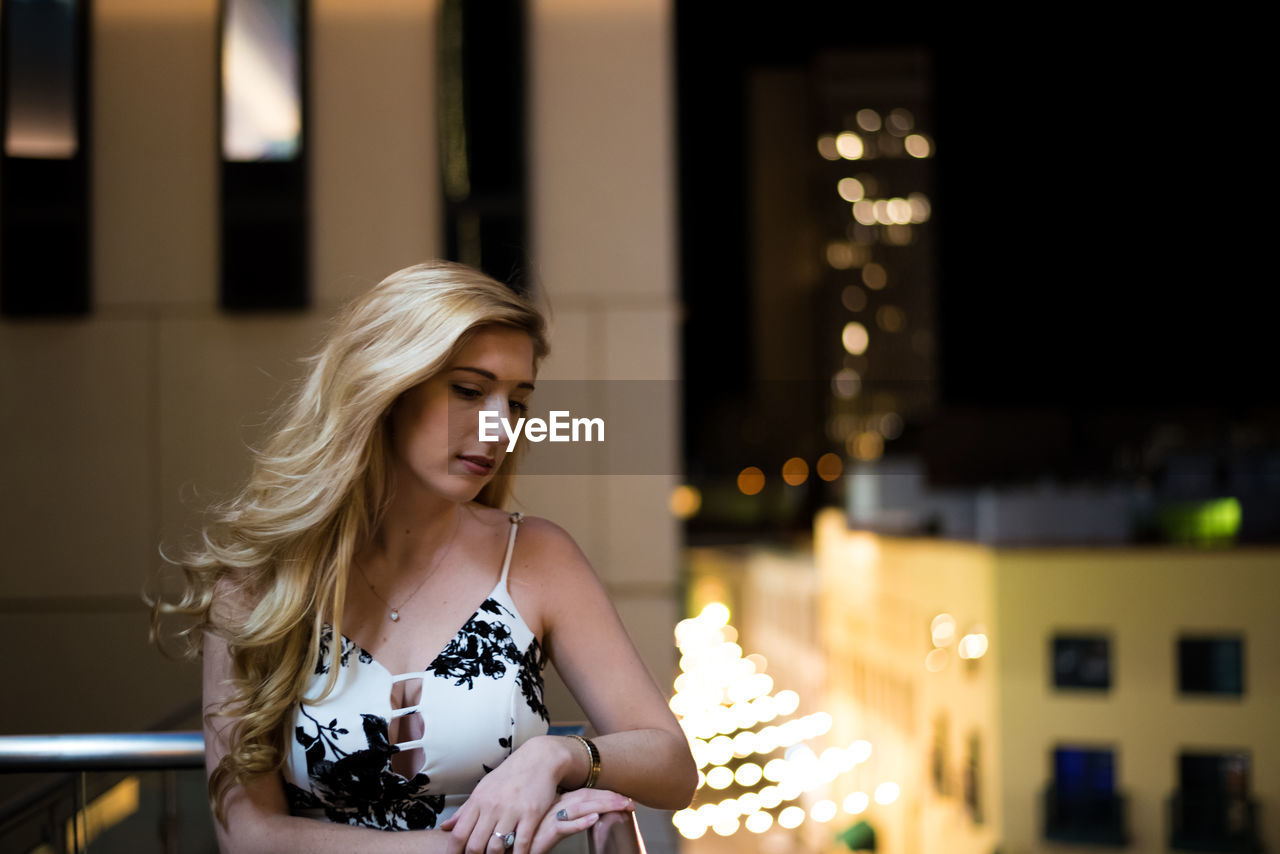 Beautiful young woman standing in balcony at night