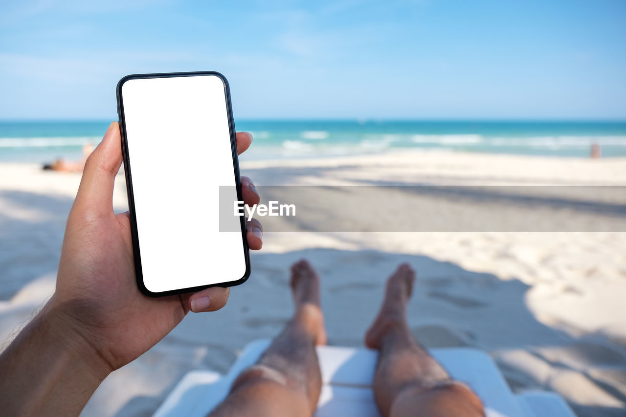 Low section of person holding mobile phone at beach