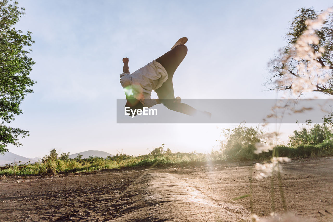 Acrobatic male jumping above ground and performing dangerous parkour trick on sunny day