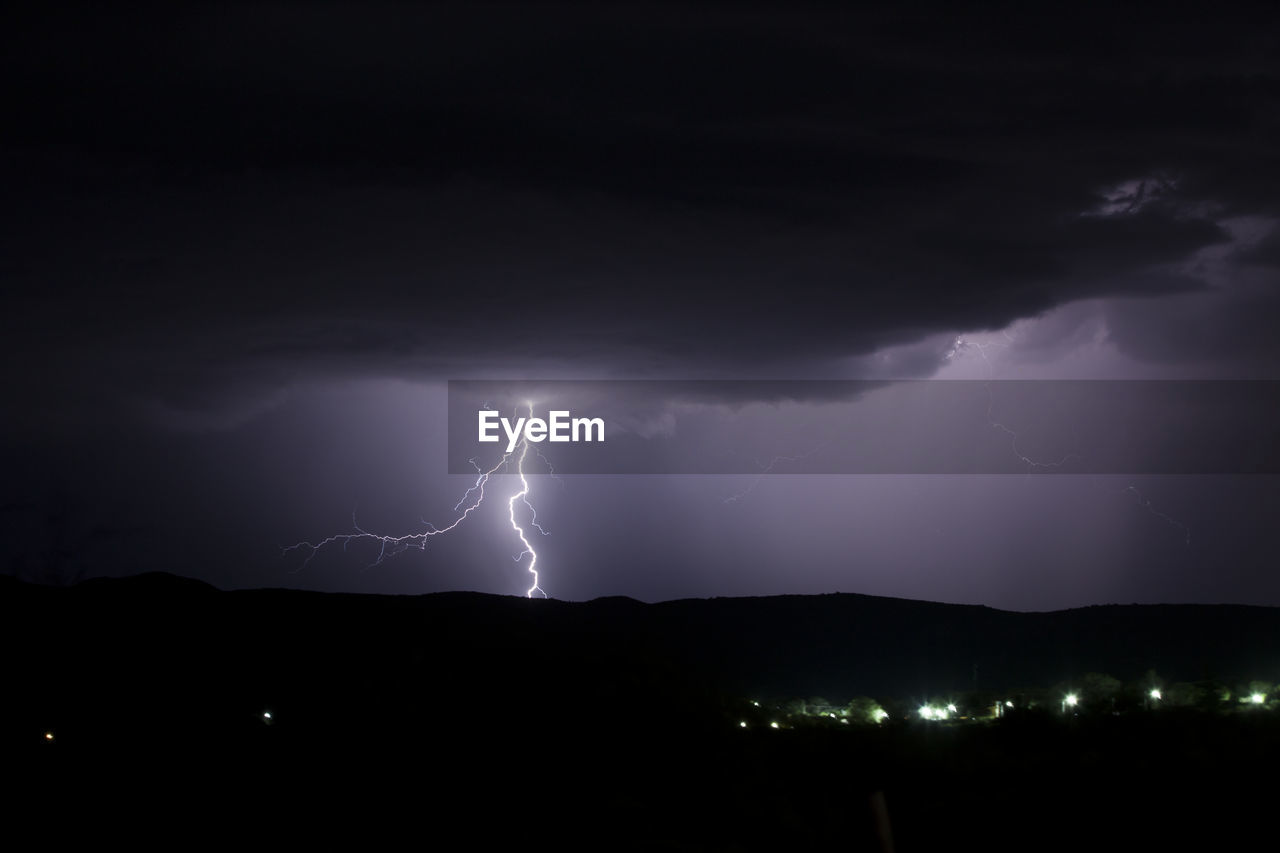 SCENIC VIEW OF LIGHTNING OVER ILLUMINATED STREET AGAINST SKY