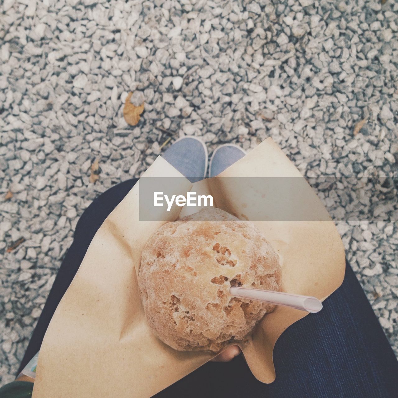 Low section of woman eating sweet food with straw over gravel