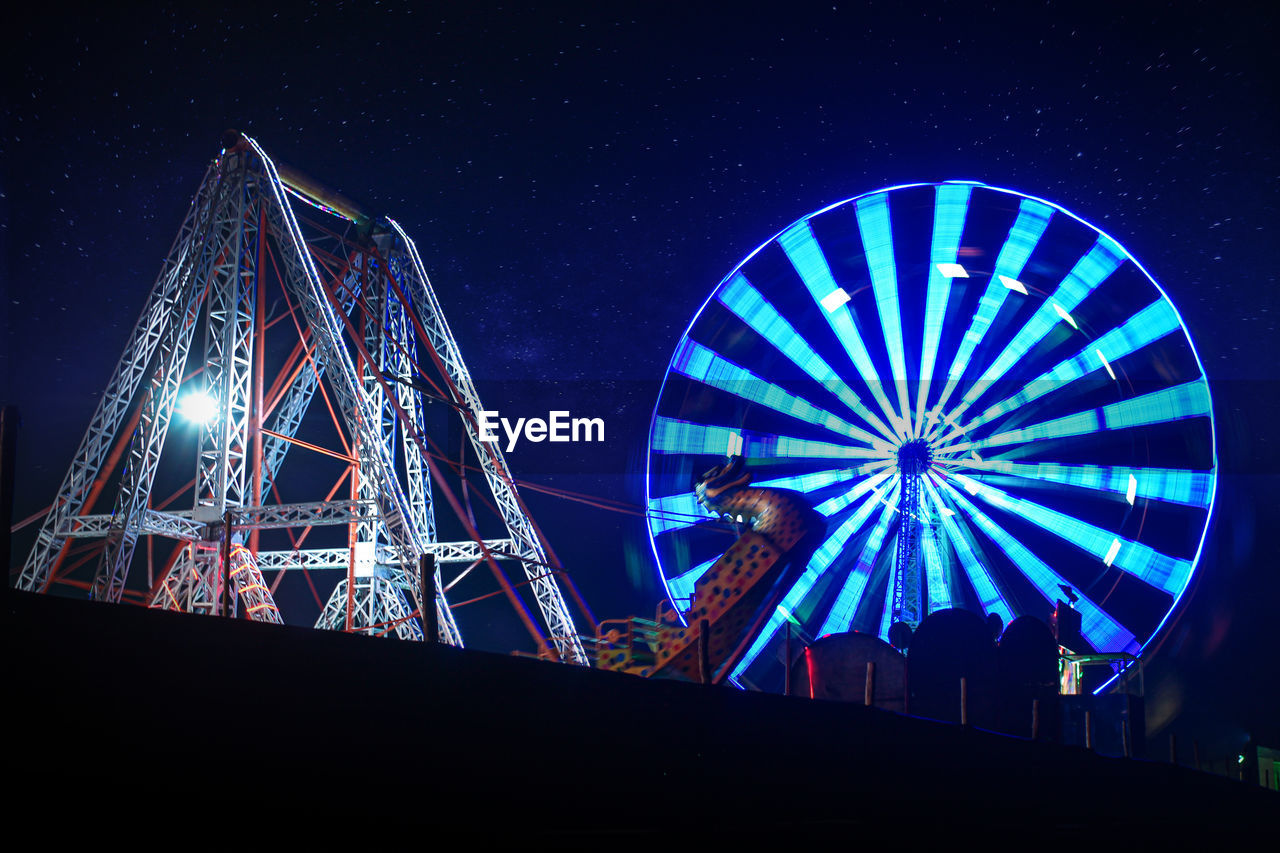 LOW ANGLE VIEW OF ILLUMINATED FERRIS WHEEL AGAINST BLUE SKY