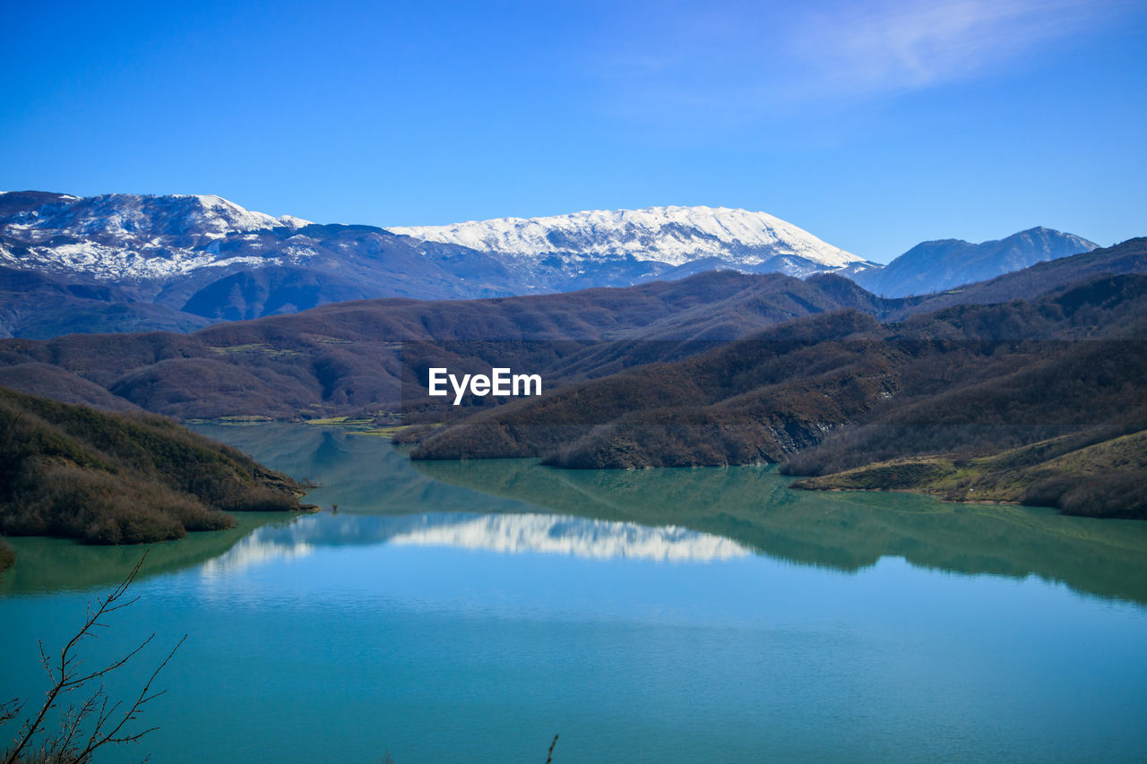 Scenic view of lake and mountains against blue sky