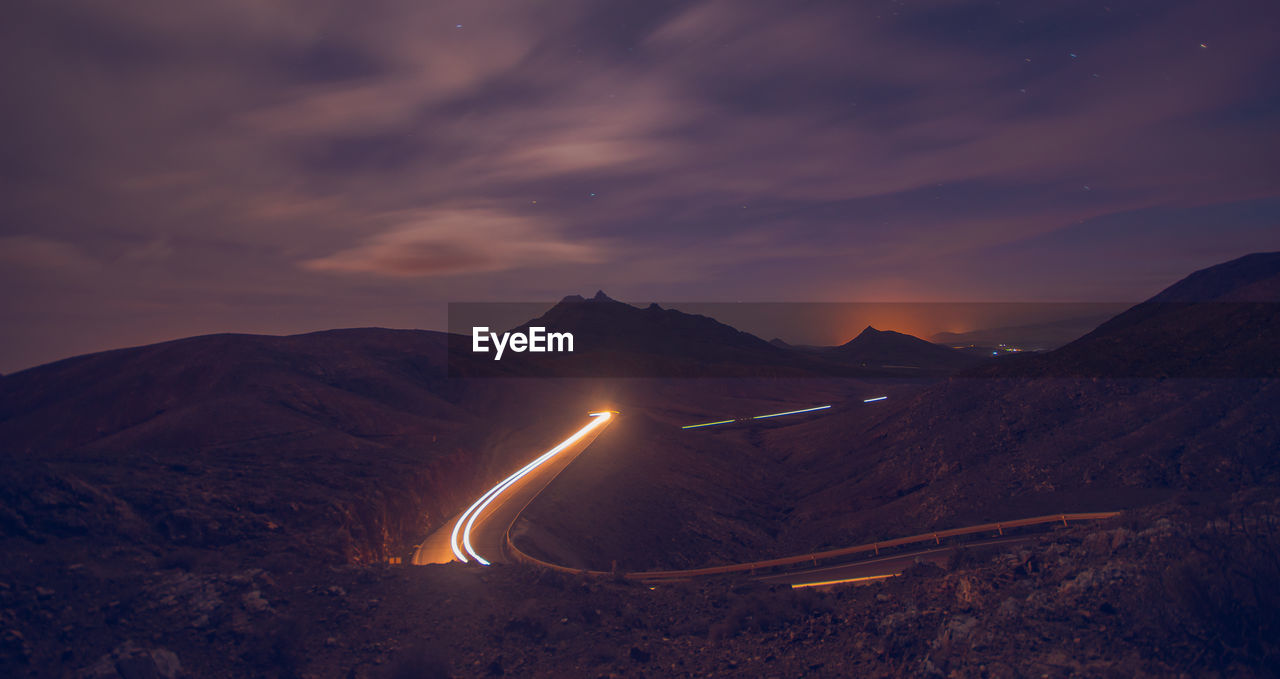 Illuminated road by mountains against sky at night