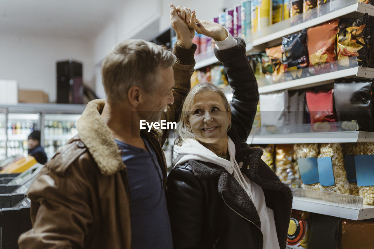 Happy mature couple dancing together with hand raised while shopping at supermarket