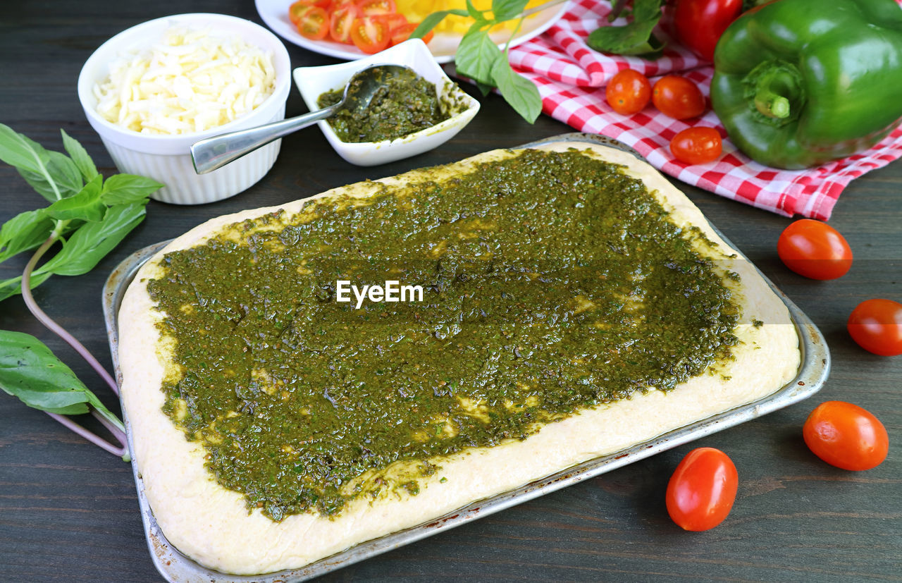 Homemade pizza dough with pesto sauce before baking in a messy kitchen