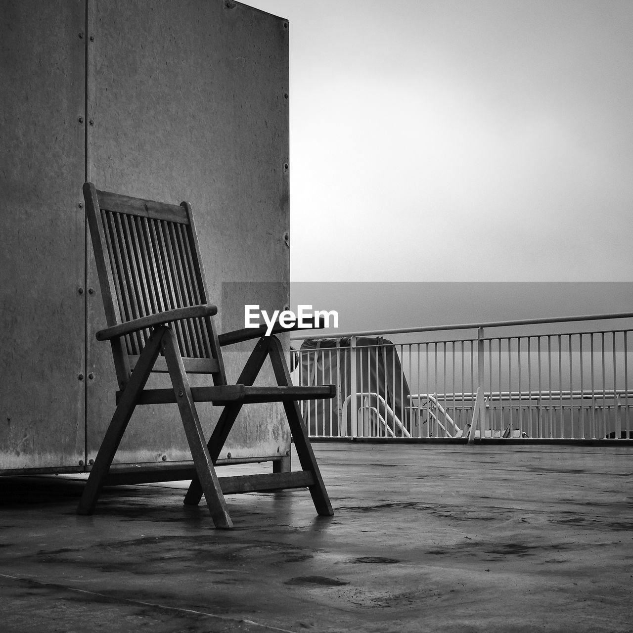 EMPTY CHAIR ON TABLE BY SEA AGAINST SKY