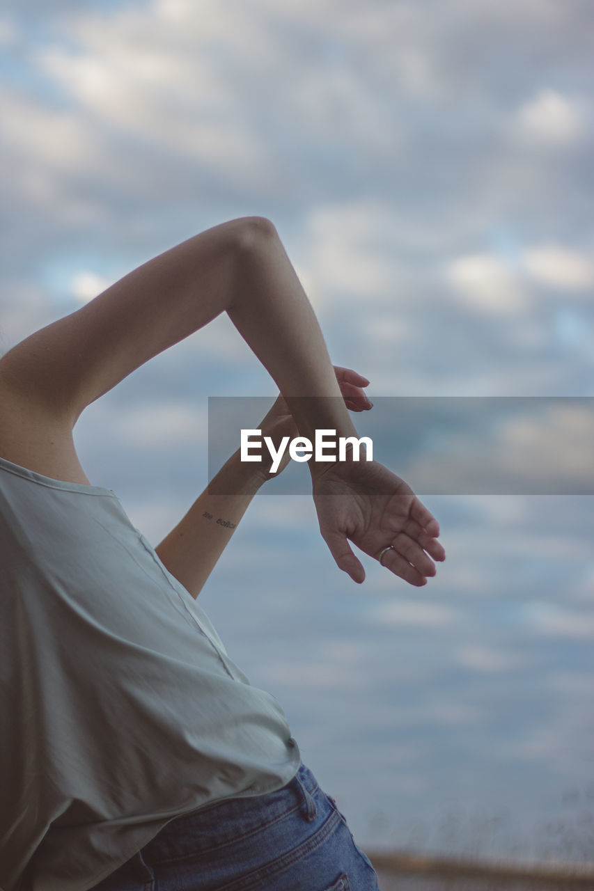 Midsection of woman dancing against cloudy sky