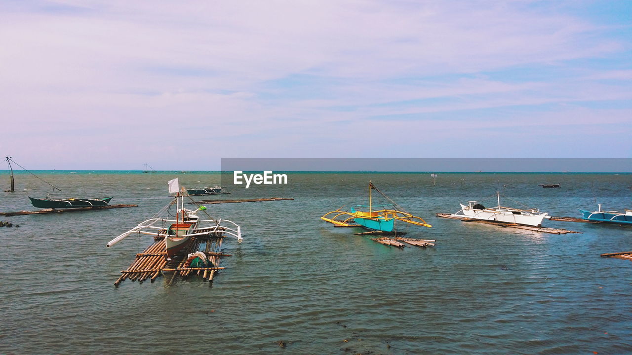 Boats in sea against cloudy sky