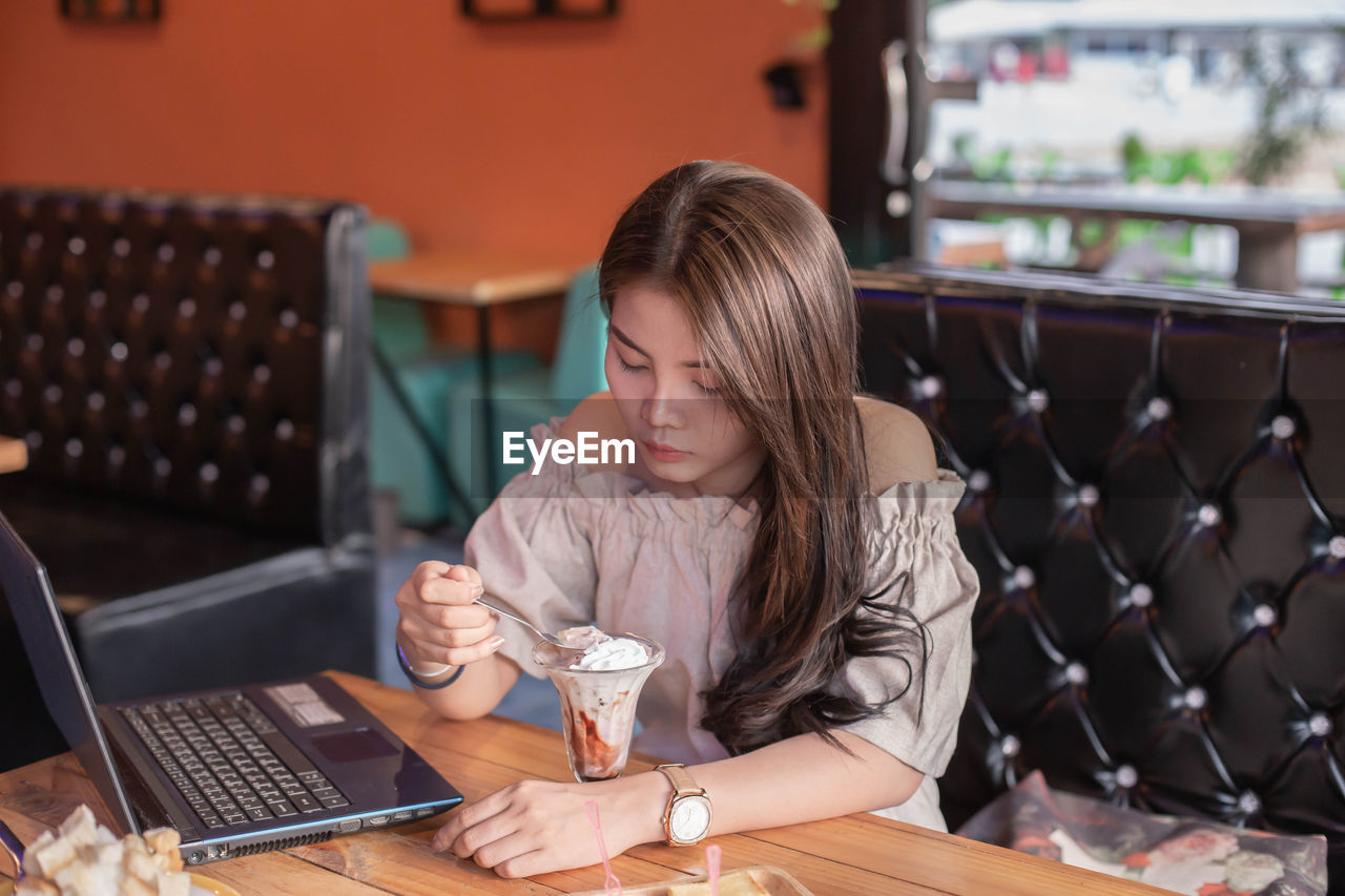 YOUNG WOMAN USING MOBILE PHONE WHILE SITTING AT TABLE