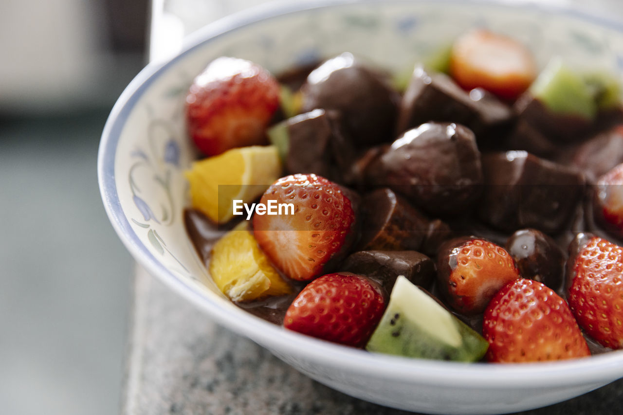 Bowl with pieces of fresh fruits and liquid chocolate in home kitchen