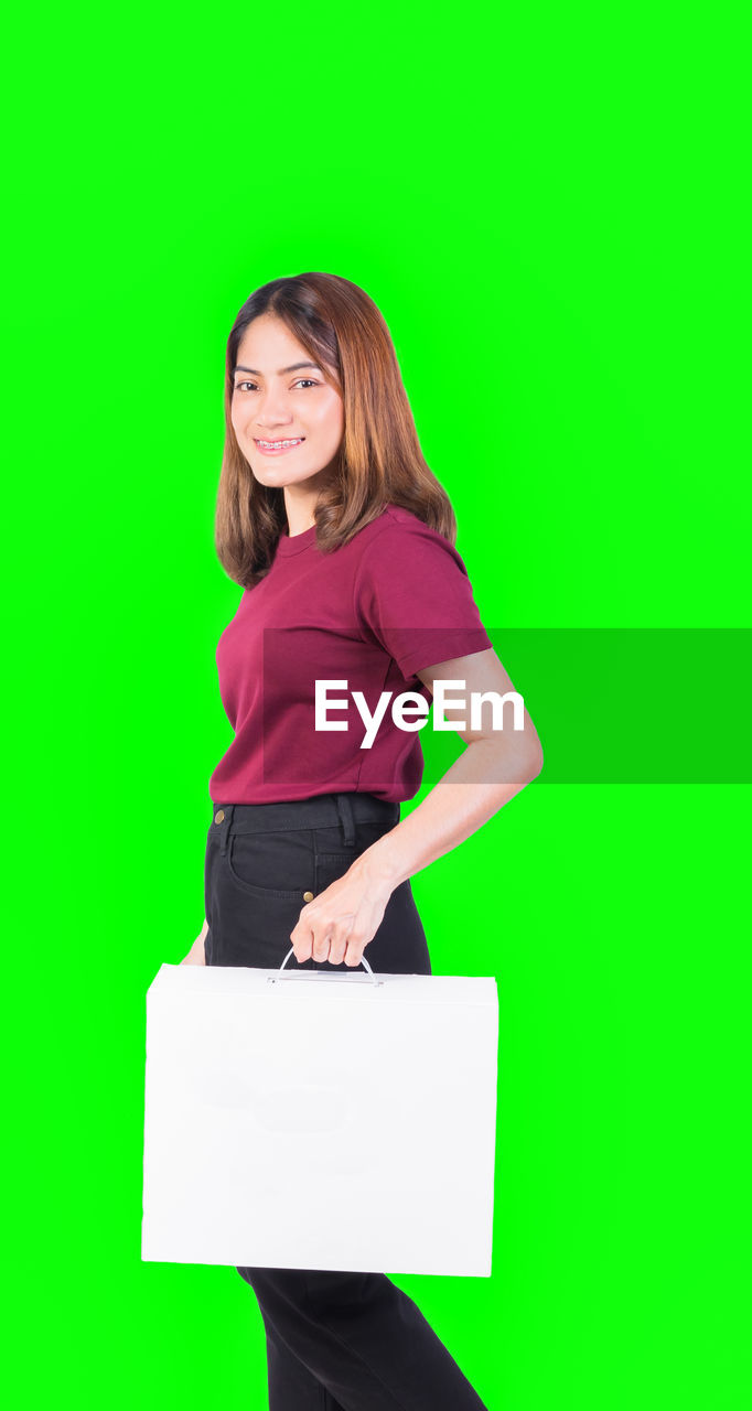 PORTRAIT OF A SMILING YOUNG WOMAN OVER GREEN BACKGROUND