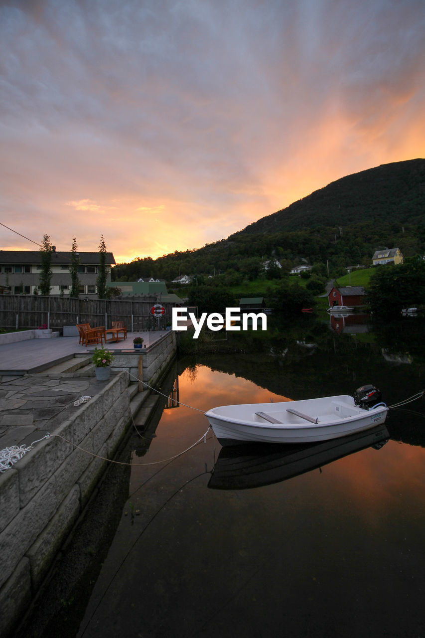 Boats moored on river by buildings against sky during sunset