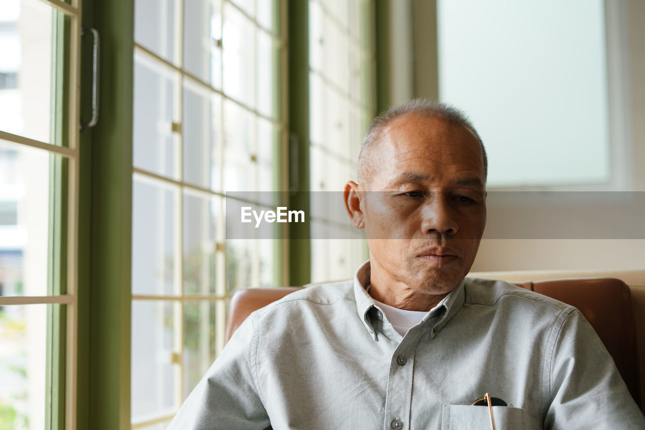 Mature man sitting on chair by window at home