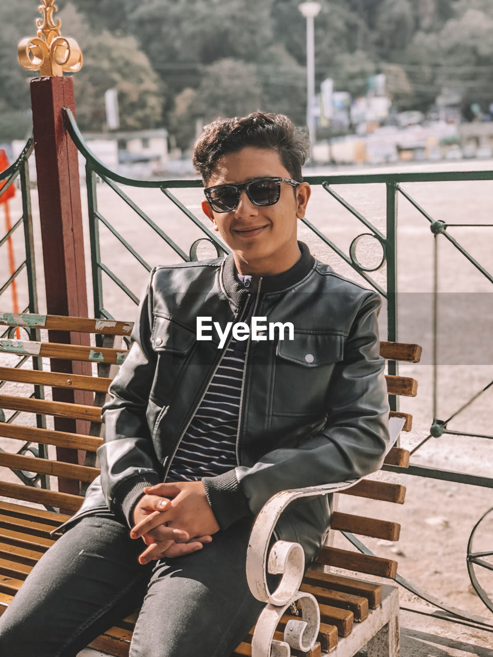 Portrait of young man sitting on bench against railing