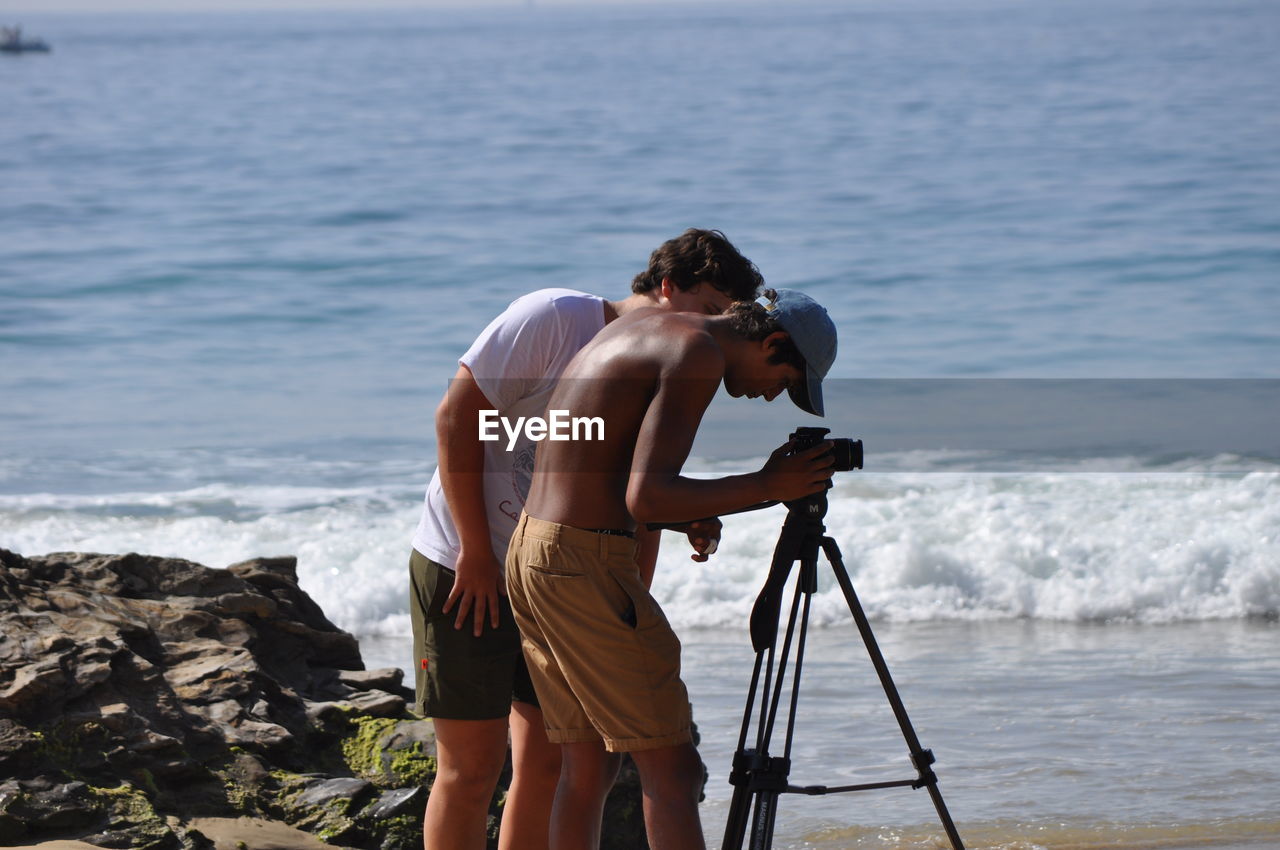 MAN PHOTOGRAPHING ON ROCK AT SEA SHORE