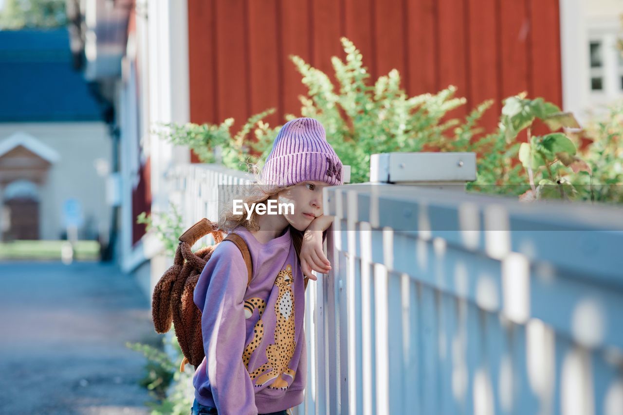 Portrait of a young girl leaning on a fence waiting for school