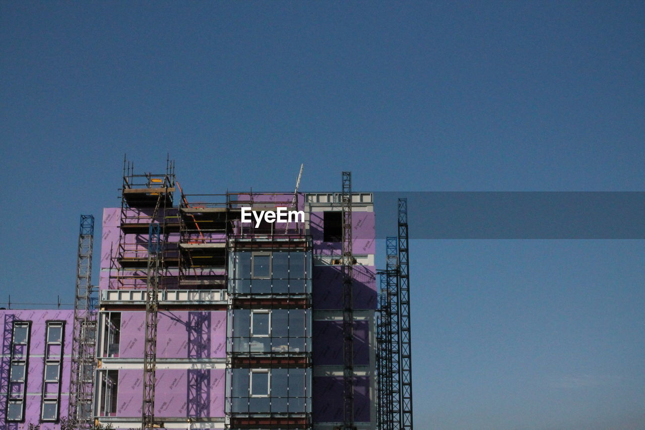 LOW ANGLE VIEW OF BUILDING AT CONSTRUCTION SITE AGAINST CLEAR BLUE SKY