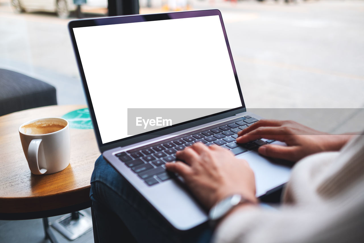 Mockup image of a woman using and typing on laptop computer keyboard with blank white desktop screen