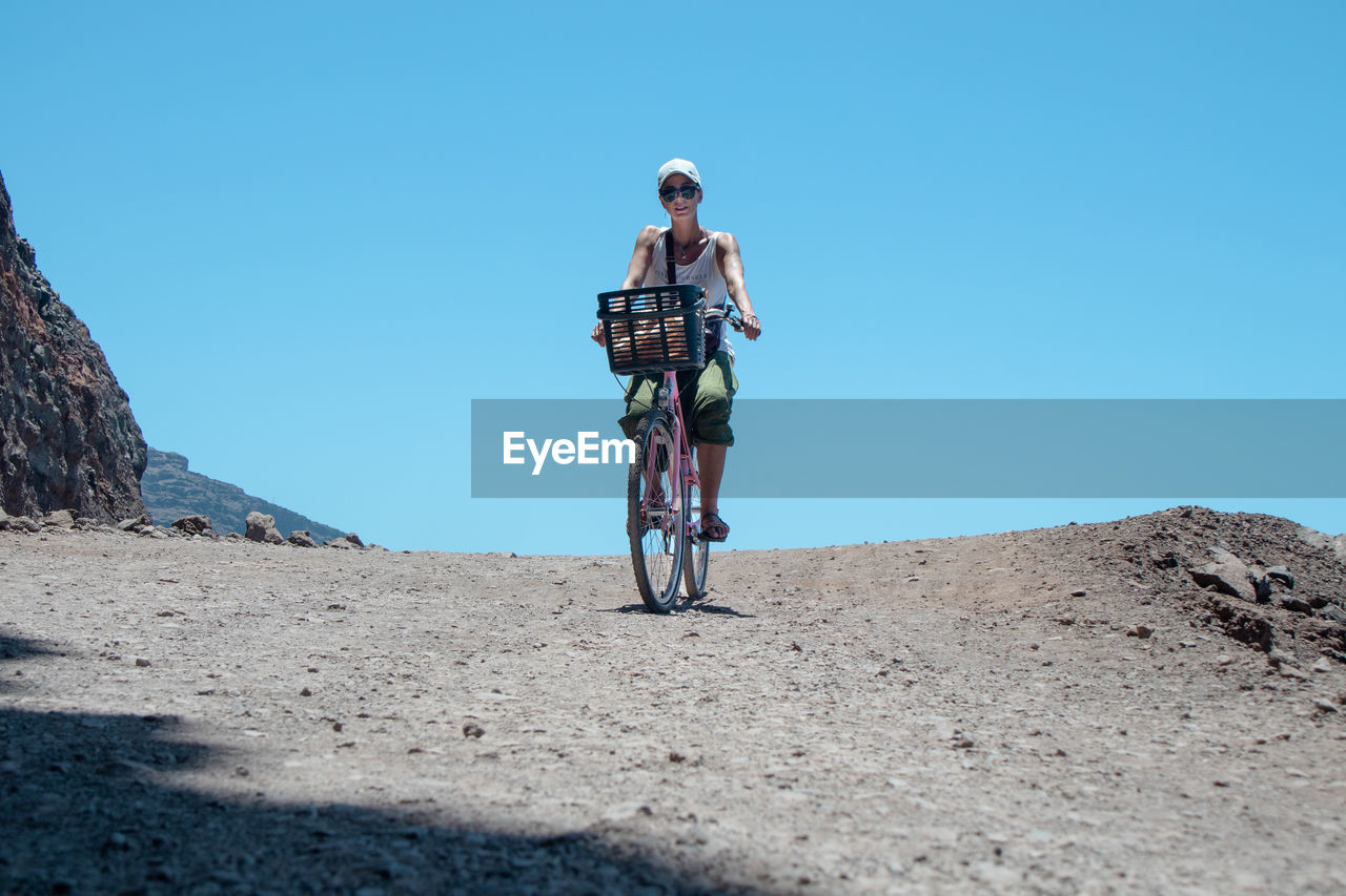 MAN RIDING BICYCLE ON ROAD AGAINST CLEAR SKY