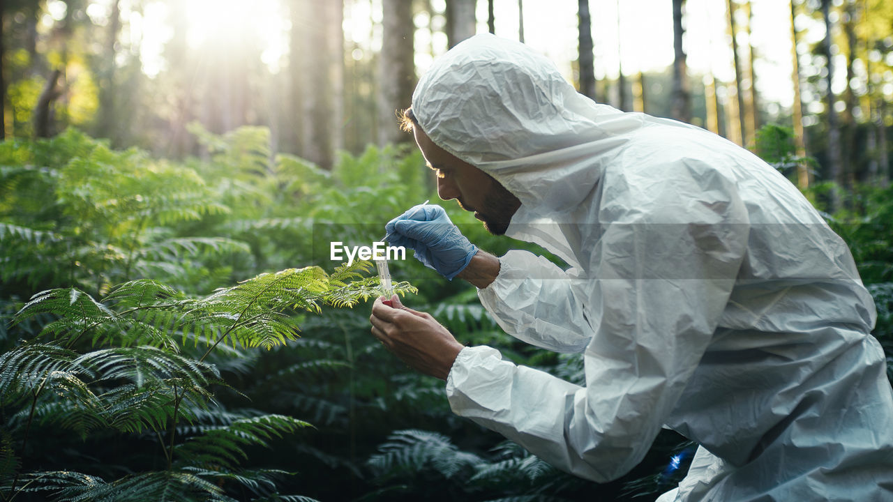 Biologist with white protective suit takes samples on new plants in the forest