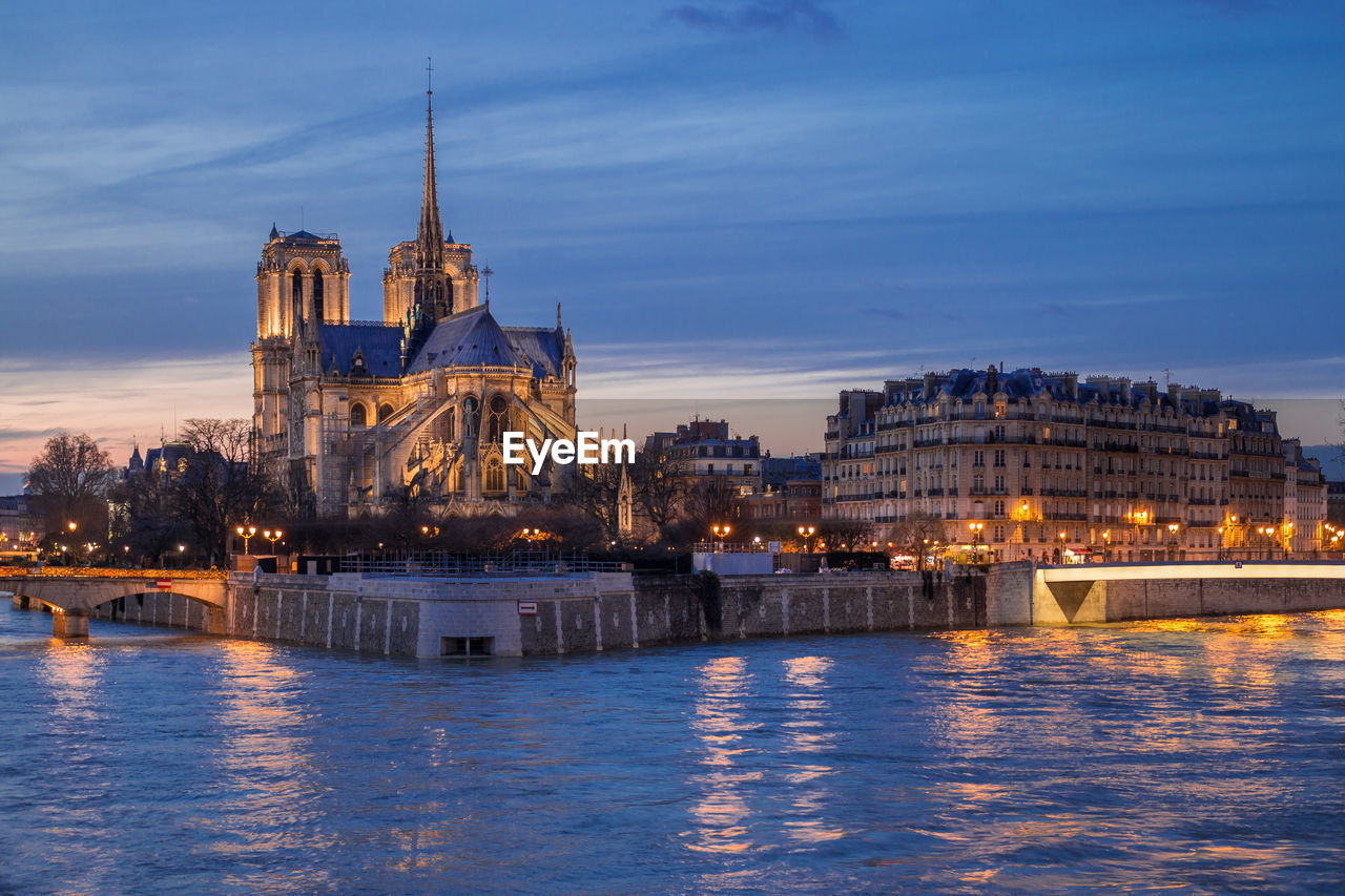 Illuminated notre dame cathedral and buildings in city against sky