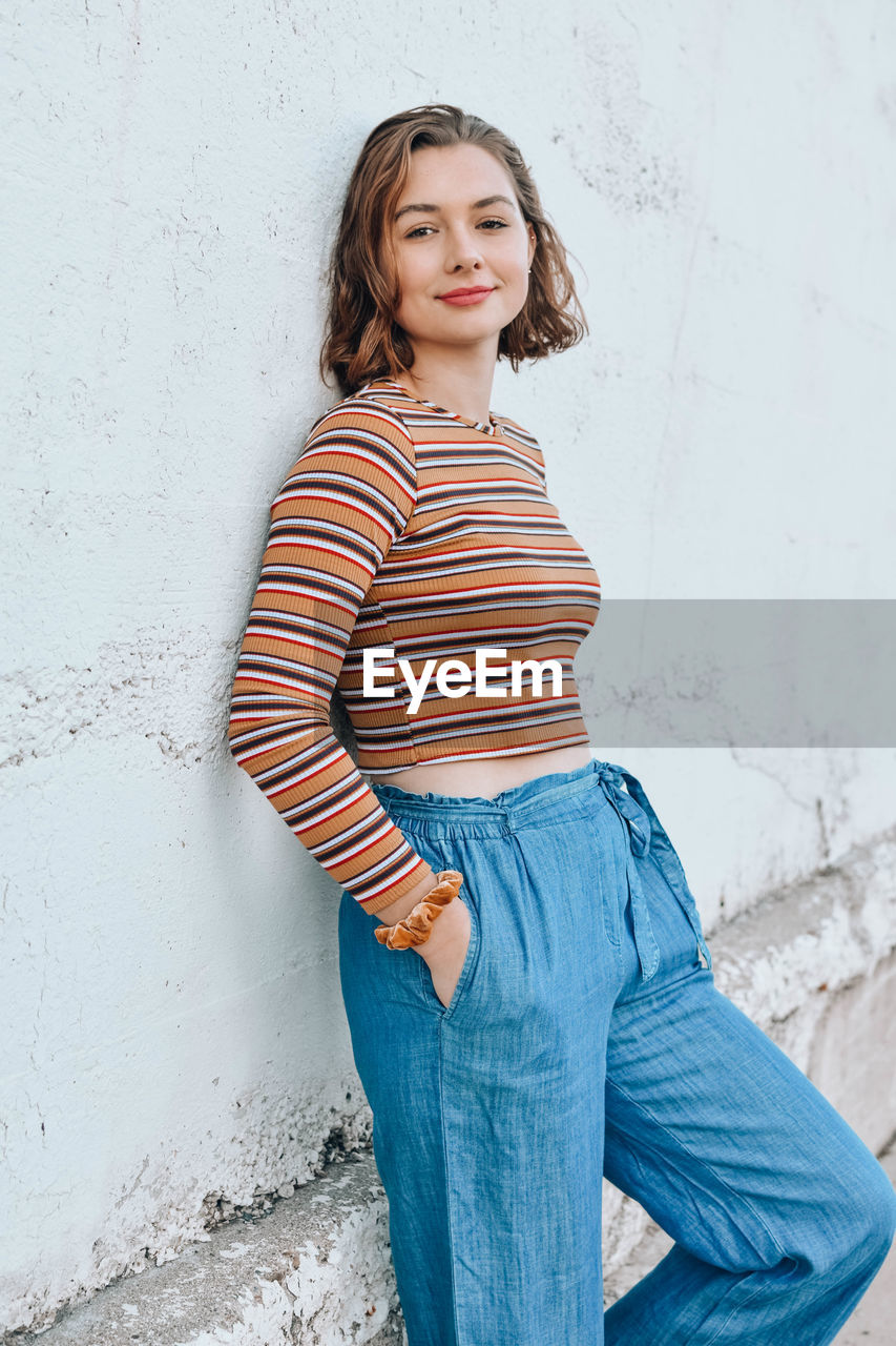 Portrait of smiling young woman standing against wall