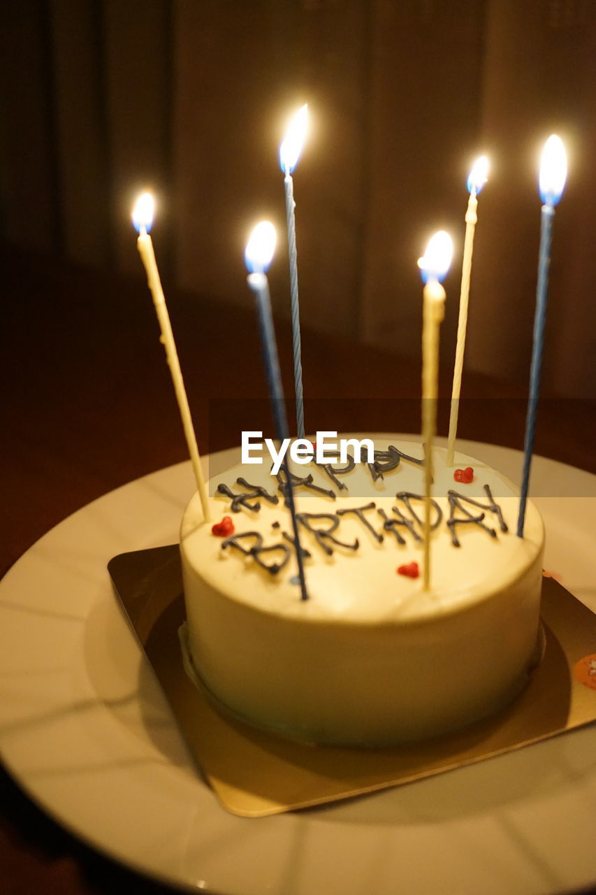 CLOSE-UP OF LIT CANDLES ON CAKE