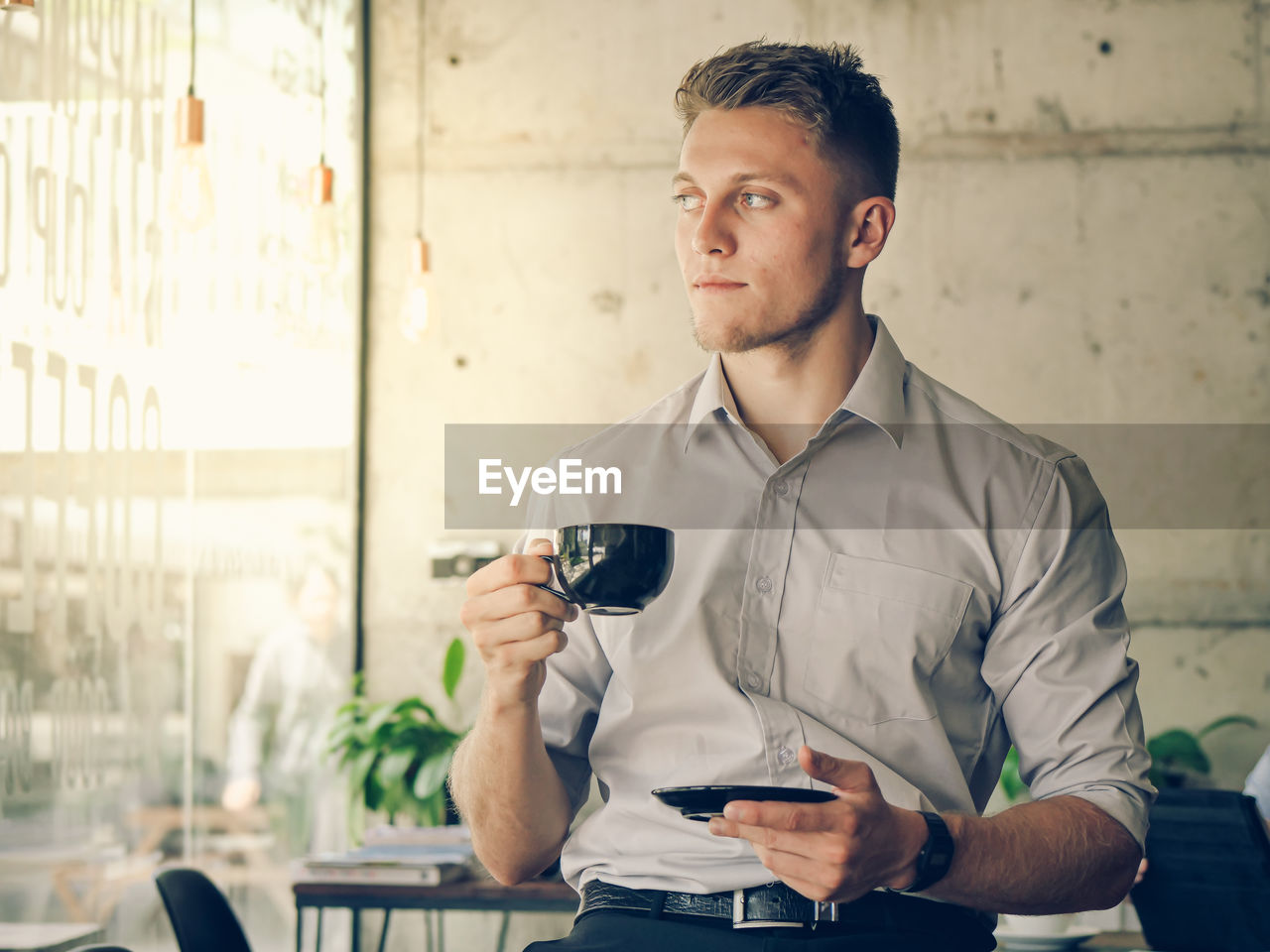 Young man looking away while holding coffee cup